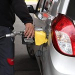 Encargado de gasolinera sirve combustible a un vehículo marcado por el aumento de precios.
