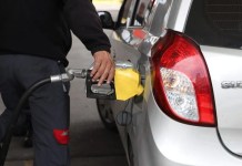 Encargado de gasolinera sirve combustible a un vehículo marcado por el aumento de precios.