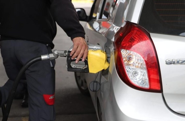 Encargado de gasolinera sirve combustible a un vehículo marcado por el aumento de precios.