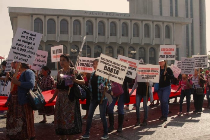 Un grupo de mujeres, con carteles, que visibilizan la violencia sexual contra la mujer, pasa enfrente del Palacio de Justicia
