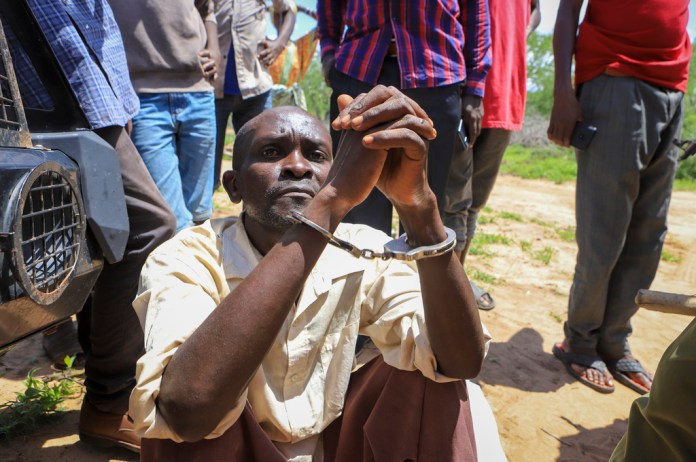 Un hombre no identificado está sentado esposado después de ser arrestado acusado de tener relación con el pastor Paul Mackenzie, en un bosque cerca de la aldea Shakahola, en el sur de Kenia, el lunes 24 de abril de 2023. 