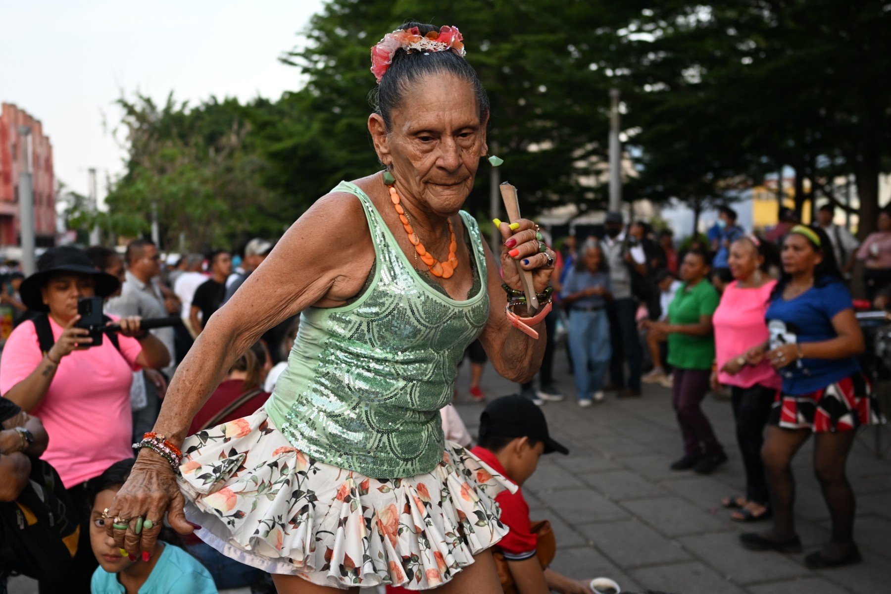 Sonia Isabel Aguilar, 75, a dancer known as Yajaira, has fun doing one of her dance routines in front of some spectators in Plaza Libertad, where people gather in the evenings to dance and play music at the historic center of San Salvador, on May 12, 2023. - The "war" against gangs, launched 14 months ago by President Nayib Bukele, has created a safe environment in the country, encouraging people to occupy public spaces.