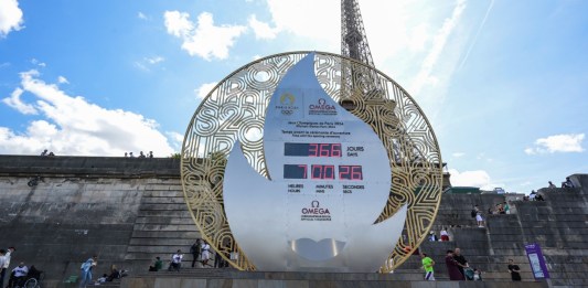 Los peatones pasan frente a un tablero que muestra la cuenta regresiva para el inicio de los Juegos Olímpicos de París 2024 frente a la Torre Eiffel en París, el 26 de julio de 2023. Foto: AFP / Alain Jocard.