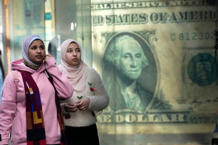 Un grupo de personas frente a un afiche con la imagen de un dólar, en El Cairo, Egipto.