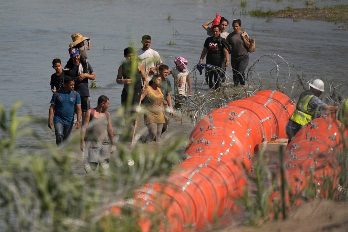Migrantes que tratan de entrar a Estados Unidos desde México se acercan a un sitio donde trabajadores están colocando unas boyas de gran tamaño para que sean utilizadas como una barrera fronteriza en el río Bravo (Grande