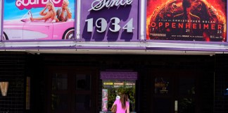 Una persona compra boletos de cine debajo de una marquesina con las películas "Barbie" y "Oppenheimer"