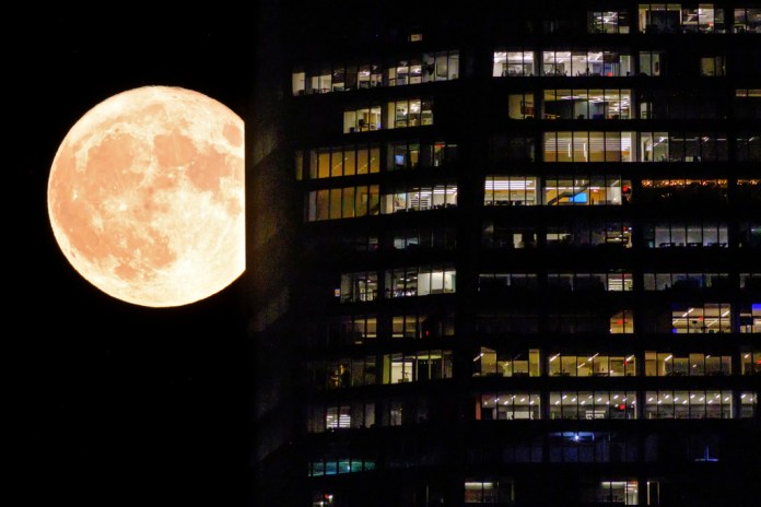 Una superluna pasa detrás de las ventanas iluminadas de un rascacielos en Nueva York.