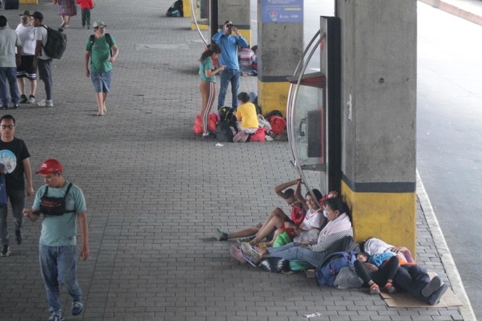 Familias en las que se observan menores de edad descansan en el lugar mientras esperan a continuar su viaje.