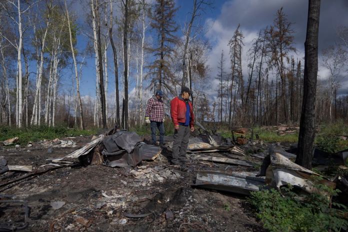 Happy Cardinal, derecha, observa los restos calcinados de su cabaña el domingo 3 de septiembre de 2023, luego de que fue destruida por incendios forestales, cerca de Fort Chipewyan, Canadá. Foto La Hora / AP