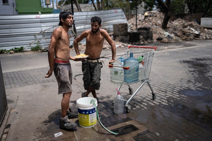 Nicolás Gonzáles, a la izquierda, y Maxi Suárez rellenan recipientes de agua de una toma de agua de la calle. Foto La Hora/AP