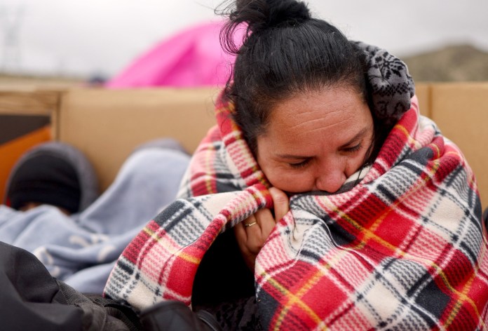 Un migrante ecuatoriano solicitante de asilo intenta mantenerse abrigado con una manta donada en un campamento improvisado poco después de cruzar la frontera, mientras espera ser procesado por la Patrulla Fronteriza de EE. UU., el 30 de noviembre de 2023 en Jacumba.