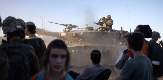 Un tanque de batalla israelí pasa junto a activistas de derecha cerca del cruce de Erez mientras se manifiestan pidiendo la construcción de asentamientos israelíes en Gaza, el 29 de febrero de 2024, en medio de las batallas en curso entre Israel y el grupo militante palestino Hamas. (Foto de Oren ZIV / AFP)