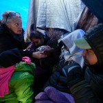 ARCHIVO - La doctora voluntaria Karen Parker, a la izquierda, toca la cabeza de un niño con fiebre mientras habla con una familia de migrantes que aguardan a ser procesados en un campamento improvisado tras cruzar la frontera desde México, el 2 de febrero de 2024, cerca de Jacumba Hot Springs, California. (AP Foto/Gregory Bull, Archivo)