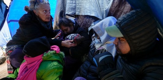 ARCHIVO - La doctora voluntaria Karen Parker, a la izquierda, toca la cabeza de un niño con fiebre mientras habla con una familia de migrantes que aguardan a ser procesados en un campamento improvisado tras cruzar la frontera desde México, el 2 de febrero de 2024, cerca de Jacumba Hot Springs, California. (AP Foto/Gregory Bull, Archivo)