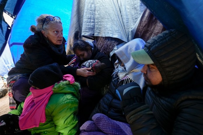 ARCHIVO - La doctora voluntaria Karen Parker, a la izquierda, toca la cabeza de un niño con fiebre mientras habla con una familia de migrantes que aguardan a ser procesados en un campamento improvisado tras cruzar la frontera desde México, el 2 de febrero de 2024, cerca de Jacumba Hot Springs, California. (AP Foto/Gregory Bull, Archivo)