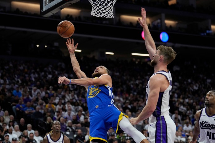 El guardia de los Golden State Warriors, Stephen Curry, dispara junto al delantero de los Sacramento Kings, Domantas Sabonis, durante la segunda mitad de un partido del torneo de baloncesto de la NBA el martes 16 de abril de 2024 en Sacramento, California (Foto AP/Godofredo A. Vásquez)