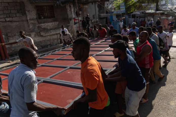 Los vecinos levantan una puerta de metal mientras trabajan para instalarla como barricada como protección contra las pandillas, en el barrio de Petion-Ville de Puerto Príncipe, Haití, el sábado 20 de abril de 2024. (Foto AP/Ramon Espinosa)