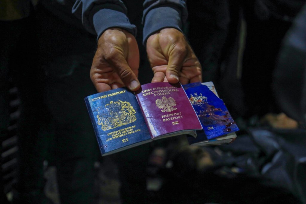 Un hombre muestra pasaportes británicos, polacos y australianos junto a los cuerpos de los trabajadores de World Central Kitchen. (Foto de AFP)