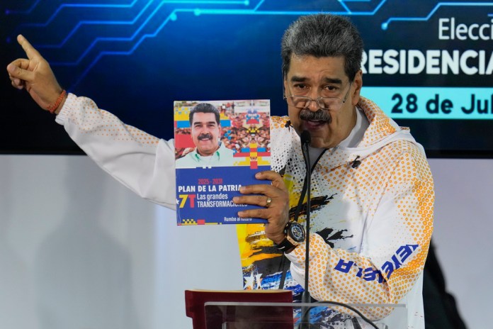 ARCHIVO - El presidente venezolano Nicolás Maduro sostiene un libro con su fotografía mientras habla en la Comisión Nacional Electoral, adonde llegó para formalizar su candidatura para postularse nuevamente a la presidencia en Caracas, Venezuela, el lunes 25 de marzo de 2024. Las elecciones están programadas para el 28 de julio. (AP Foto/Ariana Cubillos, Archivo)