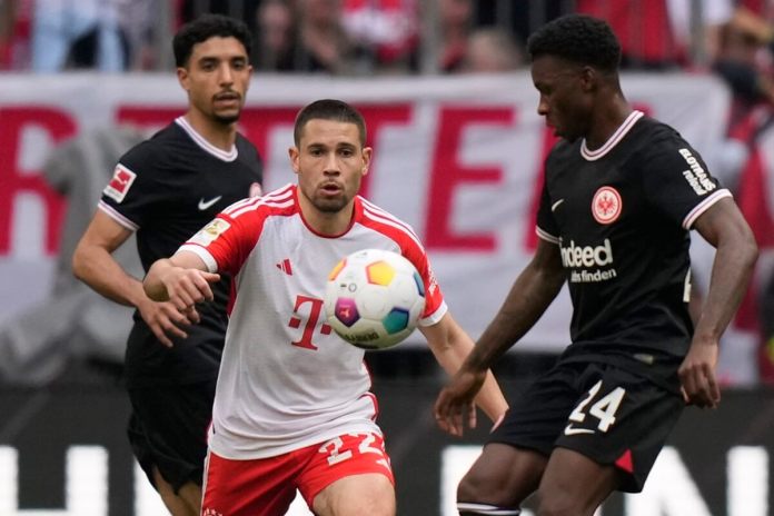 Raphael Guerreiro, izquierda, del Bayern, es desafiado por Aurelio Buta del Frankfurt durante el partido de fútbol de la Bundesliga alemana entre el Bayern Munich y el Eintracht Frankfurt, en el Allianz Arena en Munich, Alemania, el sábado 27 de abril de 2024. (Foto AP/Matthias Schrader)