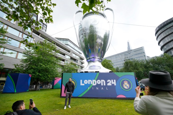 Un aficionado al fútbol posa junto a una réplica gigante del Trofeo de la Liga de Campeones en el Festival de Campeones en Potters Fields Park cerca del Tower Bridge en Londres, el jueves 30 de mayo de 2024. La final de fútbol de la Liga de Campeones entre Dortmund y Real Madrid se llevará a cabo en el estadio de Wembley. el sábado 1 de junio. (Foto AP/Kirsty Wigglesworth)