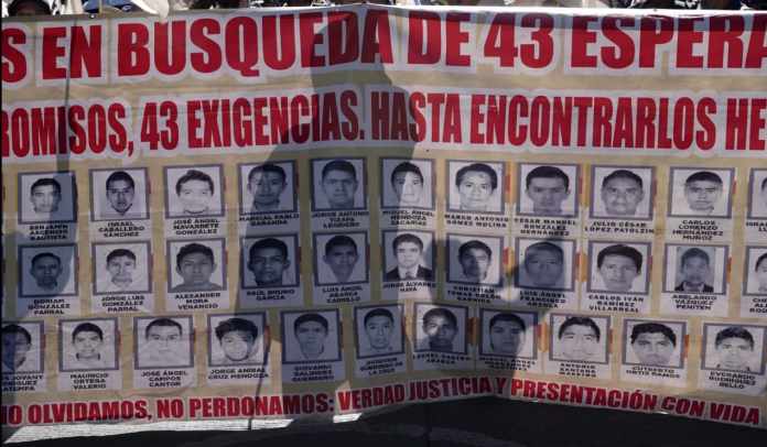 ARCHIVO - Familiares y amigos de los 43 estudiantes de Ayotzinapa desaparecidos marchan con un cartel con las fotos y el nombre de los jóvenes en el noveno aniversario de su desaparición, en Ciudad de México, el 26 de septiembre de 2023. Una corte federal mexicana decidió el jueves 9 de mayo de 2024 que ocho de los militares acusados en el caso Ayotzinapa sigan el proceso en libertad. (AP Foto/Marco Ugarte, Archivo)