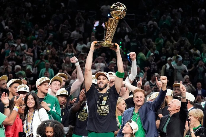 El delantero de los Boston Celtics, Jayson Tatum, sostiene, en el centro, el Trofeo del Campeonato Larry O'Brien mientras celebra con el equipo después de que ganaron el campeonato de baloncesto de la NBA con una victoria en el Juego 5 sobre los Dallas Mavericks, el lunes 17 de junio de 2024, en Boston. (Foto AP/Charles Krupa)