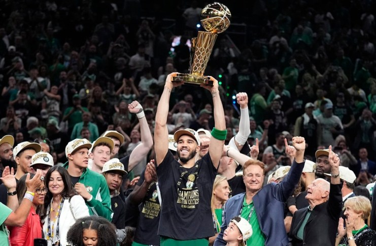 El delantero de los Boston Celtics, Jayson Tatum, sostiene, en el centro, el Trofeo del Campeonato Larry O'Brien mientras celebra con el equipo después de que ganaron el campeonato de baloncesto de la NBA con una victoria en el Juego 5 sobre los Dallas Mavericks, el lunes 17 de junio de 2024, en Boston. (Foto AP/Charles Krupa)