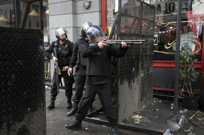 Un oficial de policía apunta con su arma a manifestantes antigubernamentales detrás de una barrera frente al Congreso donde los legisladores debaten un proyecto de ley de reforma promovido por el presidente argentino Javier Milei en Buenos Aires, Argentina, el miércoles 12 de junio de 2024. (Foto AP/Rodrigo Abd)