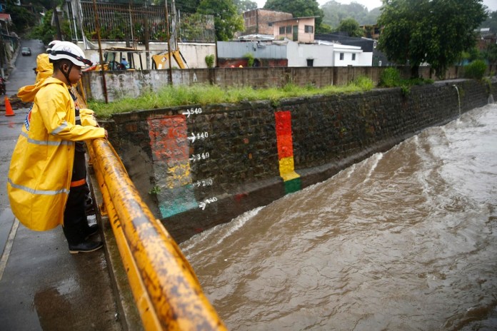Un miembro de protección civil inspecciona el caudal de un río este domingo, en San Salvador (El Salvador). EFE/Rodrigo Sura