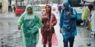 Tres personas se protegen de la lluvia con capas plásticas en el centro de San Salvador (El Salvador). EFE/Rodrigo Sura