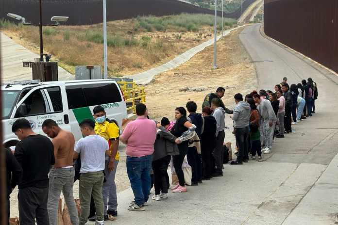 Migrantes que buscan asilo se forman mientras esperan ser procesados luego de cruzar la frontera desde México, el miércoles 5 de junio de 2024, en San Diego, California. (AP Foto/Eugene Garcia)