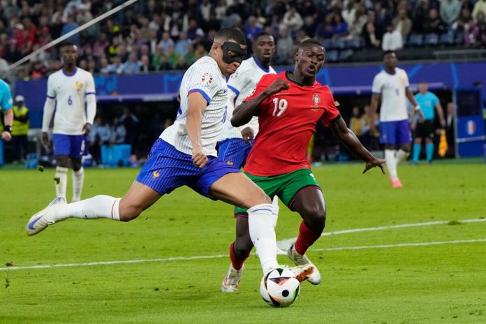 El francés Kylian Mbappe of France patea el balón mientras lo defiende el portugués Nuno Mendes en el duelo de cuartos de final de la Eurocopa el viernes 5 de junio del 2024. (AP Foto/Hassan Ammar)