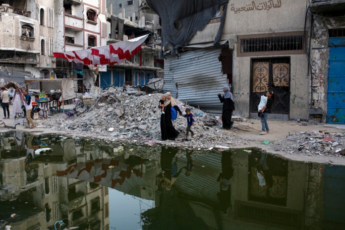 Palestinos desplazados por la ofensiva terrestre e israelí de la Franja de Gaza caminan junto a un charco oscuro de aguas residuales que fluyen a las calles en la localidad sureña de Jan Yunis, en la Franja de Gaza, el jueves 4 de julio de 2024.(AP Foto/Jehad Alshrafi)