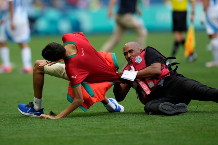 Un agente de seguridad atrapa a un hincha que invadió el campo de juego durante el encuentro de Argentina y Marruecos en el estadio Geoffroy-Guichard de Saint-Etienne, el miércoles 24 de julio de2024. (AP Foto/Silvia Izquierdo)