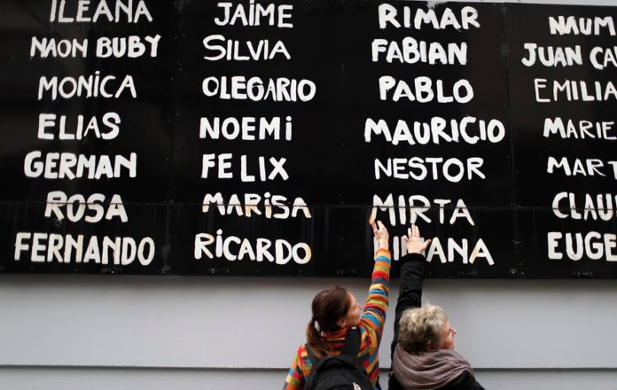 Dos mujeres tocan una tabla con nombres de personas que fallecieron en 1994 en el atentado contra el centro comunitario judío AMIA, el jueves 18 de julio de 2019, en el sitio donde ocurrió el ataque. (AP Foto/Natacha Pisarenko, archivo)