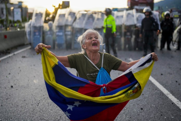 Consuelo Márquez con una bandera de Venezuela al frente de la policía que bloquea las manifestaciones contra los resultados de las elecciones que dieron por ganador a Nicolás Maduro, el día después de las votaciones en Caracas, Venezuela, el lunes 29 de julio de 2024. (AP Foto/Matías Delacroix)
