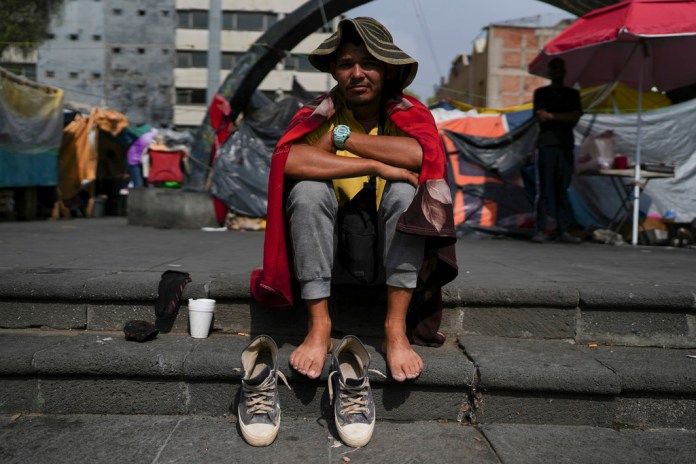 El inmigrante venezolano Cristo Pérez, de 33 años, sentado al sol en un campamento de migrantes frente a la Iglesia de La Soledad en la Ciudad de México, el miércoles 31 de julio de 2024. (Foto AP/Marco Ugarte)