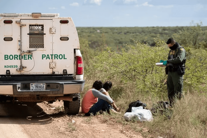 Un oficial de la Patrulla Fronteriza revisa los documentos de dos migrantes que recién cruzaron la frontera. Foto: CBP.