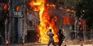 Unos hombres corren frente a un centro comercial que fue incendiado durante una manifestación contra la primera ministra Sheikh Hasina y su gobierno, en Dacca, Bangladesh, el domingo 4 de agosto de 2024. (Foto AP/Rajib Dhar) Photo Details