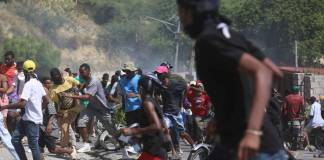 Un grupo de personas huye del gas lacrimógeno disparado por la policía para dispersar a los manifestantes que exigen a la policía y al primer ministro que actúen de inmediato contra las pandillas, en Puerto Príncipe, Haití, el lunes 19 de agosto de 2024. (AP Foto/Odelyn Joseph)