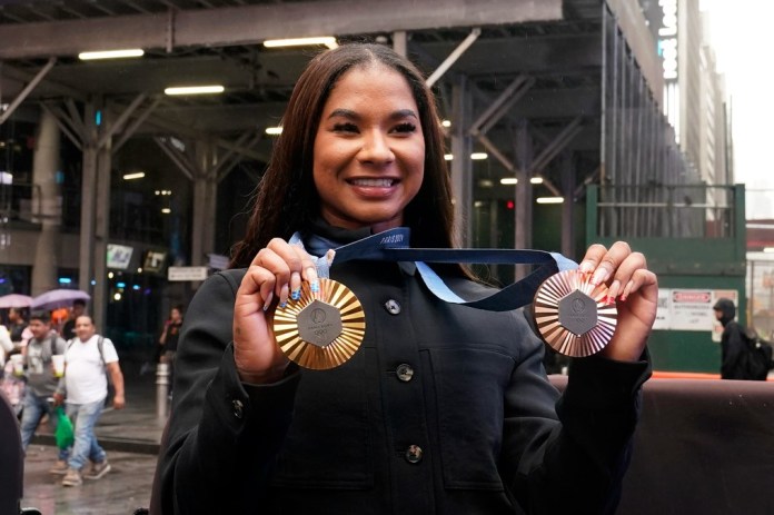 La gimnasta estadounidense y medallista olímpica Jordan Chiles muestra sus medallas tras el cierre del Nasdaq MarketSite, en Times Square, Nueva York, el jueves 8 de agosto de 2024. (AP Foto/Richard Drew)