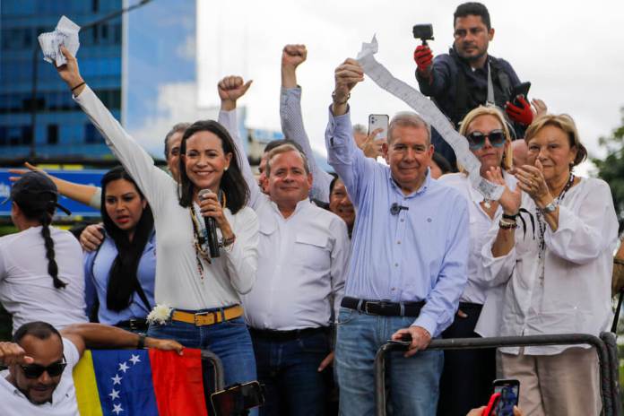 La líder opositora María Corina Machado, a la izquierda, y el candidato opositor Edmundo González sostienen actas de votación desde lo alto de un camión durante una protesta. (AP Foto/Cristian Hernández)