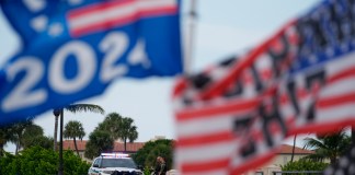 Policías resguardan un puente ubicado a un costado de la finca Mar-a-Lago del expresidente Donald Trump mientras un simpatizante ondea banderas para expresar su apoyo a Trump, un día después de un aparente intento de asesinato en su contra, el lunes 16 de septiembre de 2024, en Palm Beach, Florida. (AP Foto/Rebecca Blackwell)