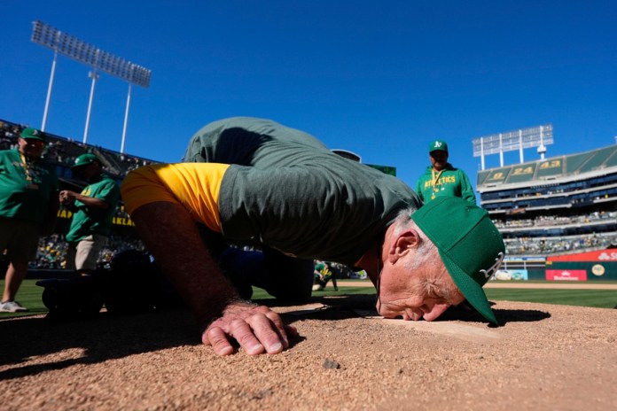 El fotógrafo del equipo de los Atléticos de Oakland, Michael Zagaris, besa el montículo del lanzador después de un partido de béisbol contra los Rangers de Texas en Oakland, California, el jueves 26 de septiembre de 2024. (AP Foto/Godofredo A. Vásquez)