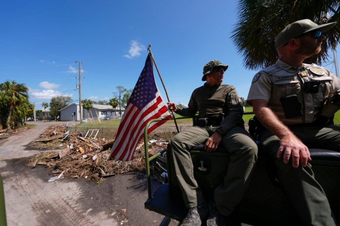 Agentes de la ley de la Comisión de Pesca, Vida Silvestre y Conservación de Florida, sostiene una bandera estadounidense que estaba en el suelo entre escombros después del huracán Helene. (Foto AP/Gerald Herbert)