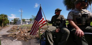 Agentes de la ley de la Comisión de Pesca, Vida Silvestre y Conservación de Florida, sostiene una bandera estadounidense que estaba en el suelo entre escombros después del huracán Helene. (Foto AP/Gerald Herbert)