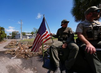 Agentes de la ley de la Comisión de Pesca, Vida Silvestre y Conservación de Florida, sostiene una bandera estadounidense que estaba en el suelo entre escombros después del huracán Helene. (Foto AP/Gerald Herbert)