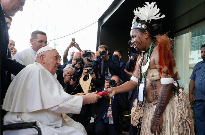 El papa Francisco entrega un regalo a un intérprete de bailes tradicionales a su llegada a APEC Haus, en Puerto Moresby, Papúa Nueva Guinea, el 7 de septiembre de 2024. (AP Foto/Mark Baker)