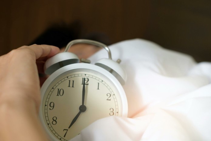 Persona sosteniendo un reloj acostado en la cama.Foto: Pexels